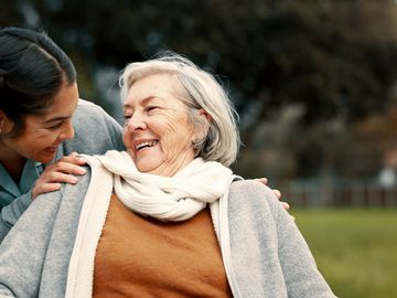 A young woman joyfully interacts with an elderly woman outdoors.