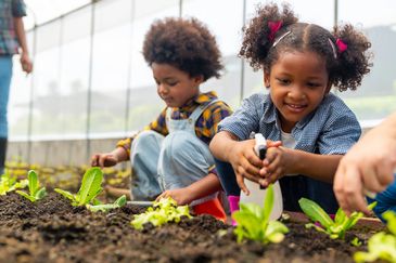 Two children gardening and caring for young plants in a greenhouse.