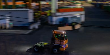 A small orange industrial vehicle moves through a busy yard at night.