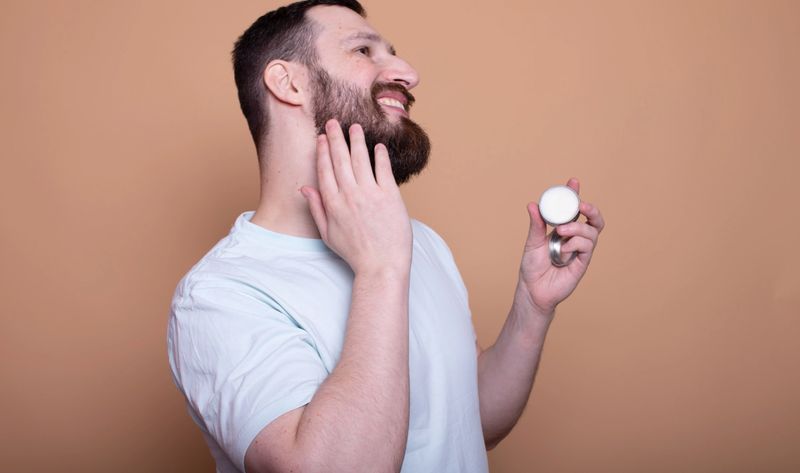 Bearded man presenting balm fo beard on beige background.