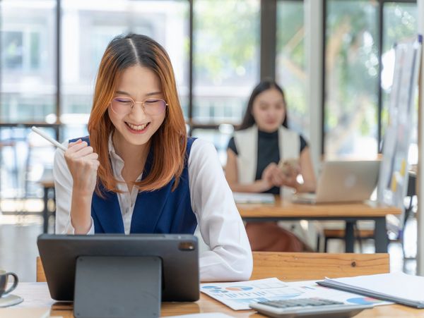 A woman happily working on a tablet in a bright office.
