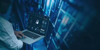 Person using laptop with cybersecurity interface in data center.