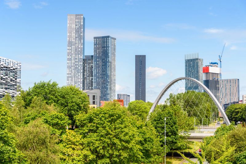 High rise buildings in Manchester on a sunny, summer day. A modern bridge over a thoroughfare leading to city centre is in foreground. England, UK,