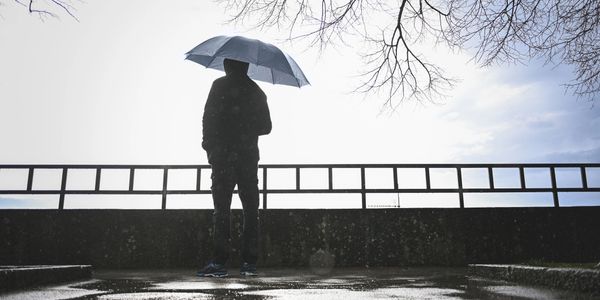 A person holding an umbrella stands by a railing on a rainy day.