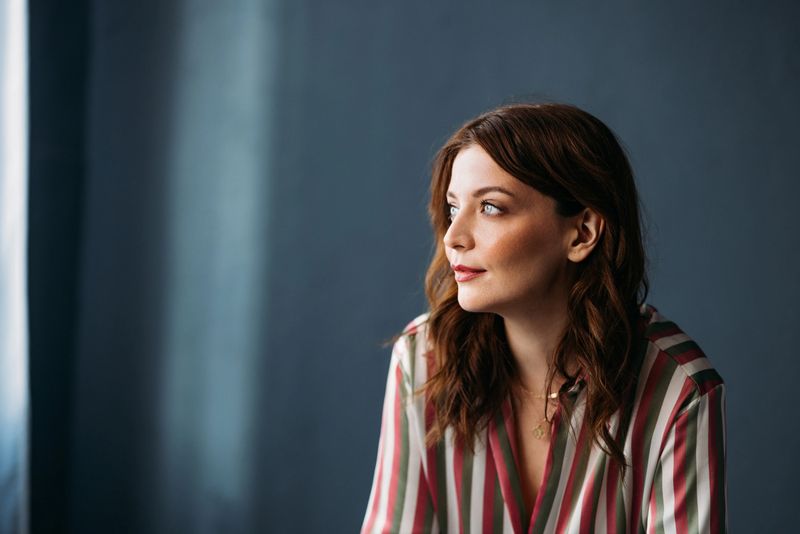 Contemplative young woman with wavy hair, gazing away, striped blouse, natural light, serene, thoughtful, indoors