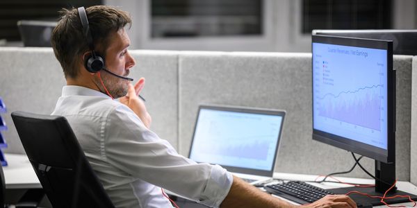 Man in headset analyzing financial graphs on dual monitors in an office.