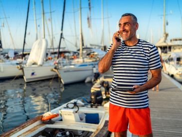Smiling man in striped shirt talking on phone at marina with boats.