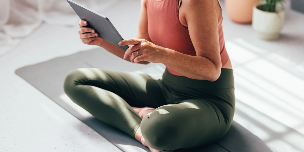 Person sitting cross-legged on a mat using a tablet.