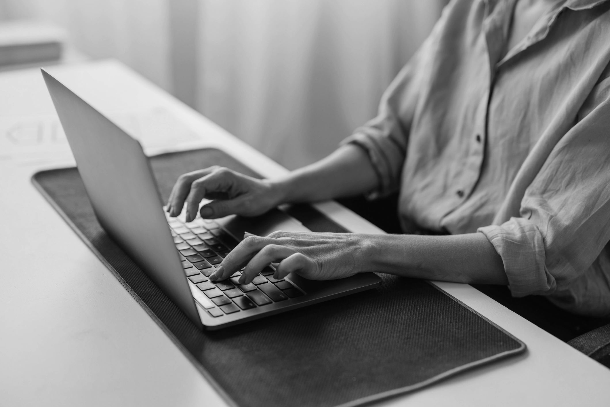 Person typing on a laptop at a yellow desk with a black mat.