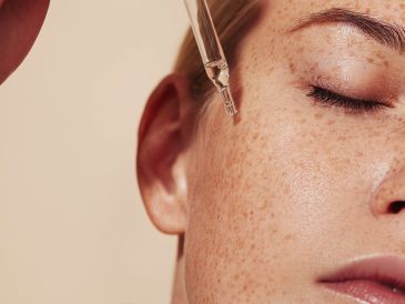 Close-up of a woman applying facial serum with a dropper near her eye.