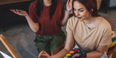 Two women painting together, one focusing on the artwork.