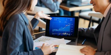 Two people discussing stock market trends on a laptop.