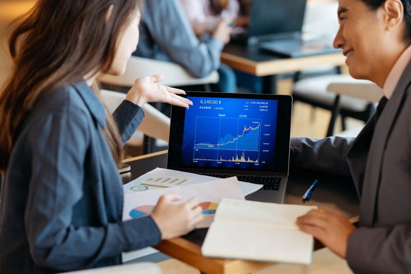 Asian Chinese businessman and businesswoman team discuss and analyzing stock market data on laptop computer