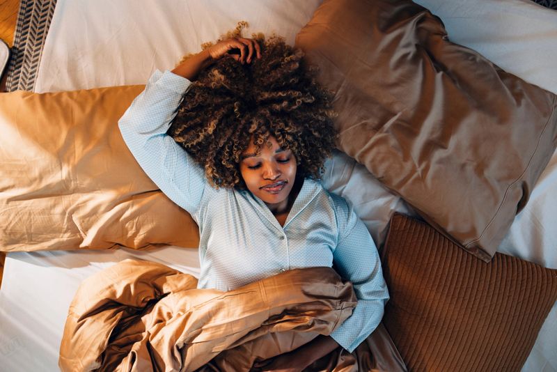 Overhead view of a peaceful young woman lying comfortably in bed with closed eyes, exuding calmness and tranquility indoors.