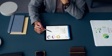 Person analyzing charts and graphs on a tablet at a desk.
