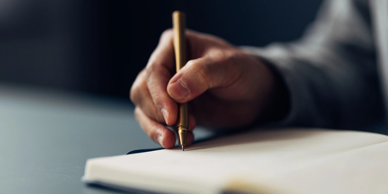 A hand holding a pen poised to write in a notebook.