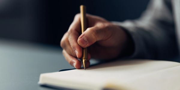 Person writing in a notebook with a pen.