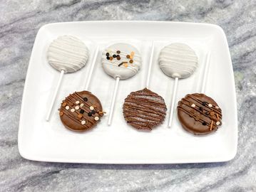 Chocolate and white chocolate covered cookie pops with sprinkles on a white plate.