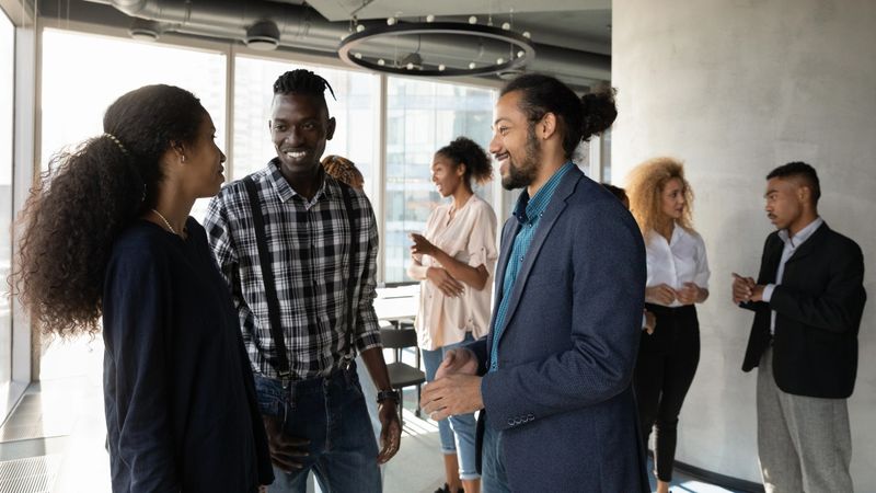Discussing affairs. Millennial black man agent broker speak hold pleasant business conversation with diverse colleagues. Young smiling mixed race male manager talk to clients couple at office space