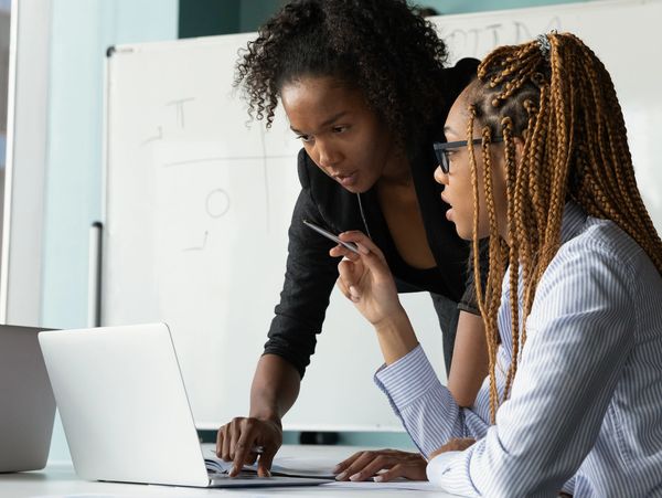 Two women collaborating over a laptop in a modern office.