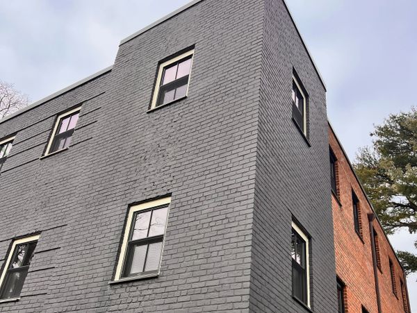 Gray and red brick building with multiple windows under an overcast sky.