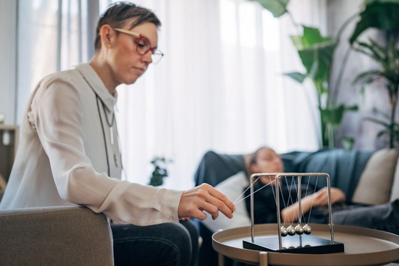 A therapist, seated attentively, is conducting a hypnosis session with a client who is lying comfortably on a couch. The serene and well-lit room provides an ideal environment for therapy.