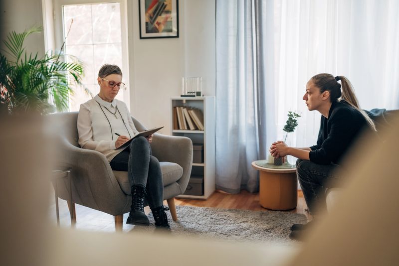 A therapist, seated comfortably, attentively listens and provides advice to an individual seeking guidance. The calm and well-lit environment fosters a space of trust and openness.