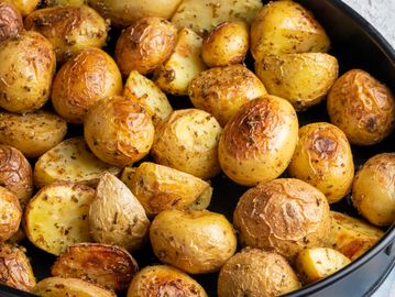 Golden roasted baby potatoes seasoned with herbs in a black dish.