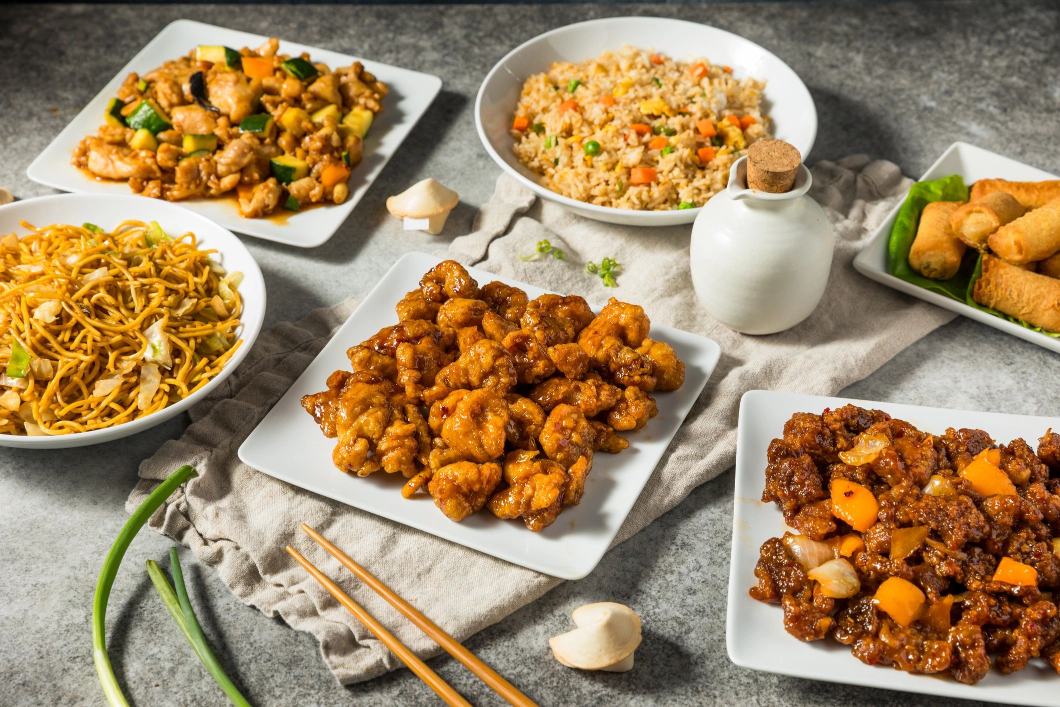 Chinese food dishes on plates with chopsticks and green onions.