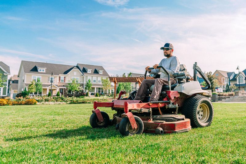Hispanic Man Driving a Professional Riding Lawnmower for a Landscaping Company at an Apartment Complex or Public Park on a Sunny Morning in the Summer, USA