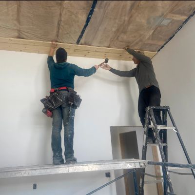 Two workers installing wooden panel on ceiling during construction.