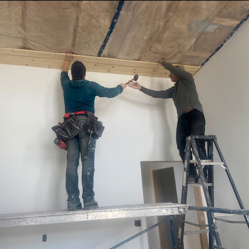 Senior and young man stand on scaffolding and build tongue and groove ceiling together