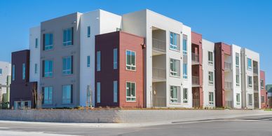 Modern apartment complex with white and reddish-brown exterior under clear blue sky.