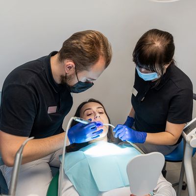 Dentist and assistant treating a patient wearing masks and gloves.