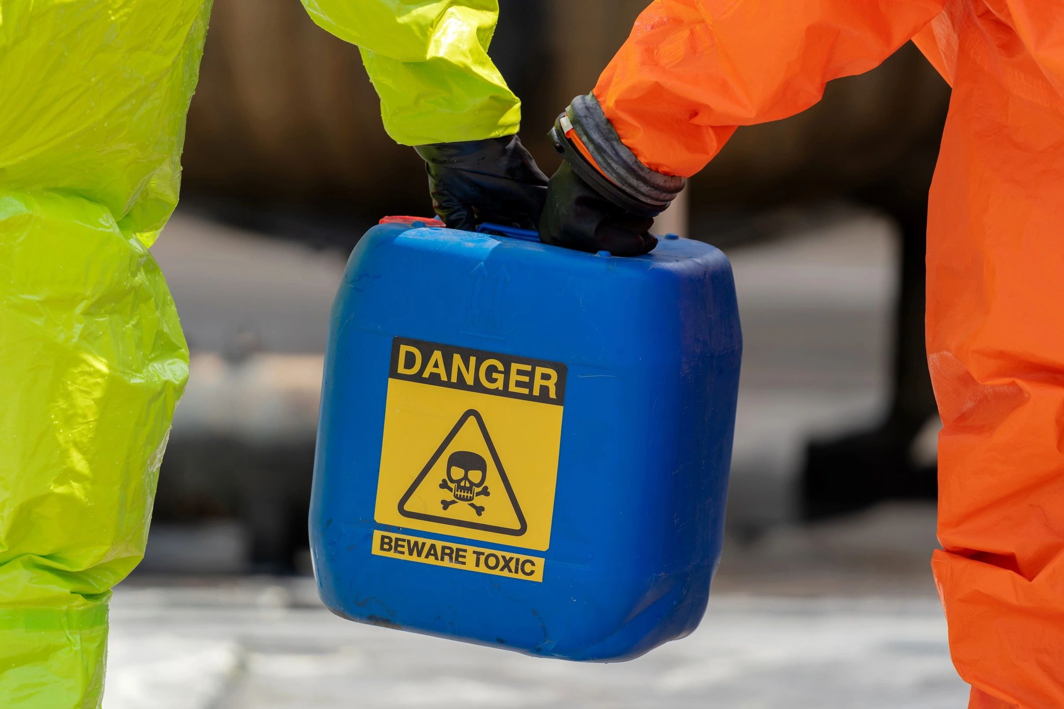 Worker in protective equipment handling a warning-labelled chemical container.