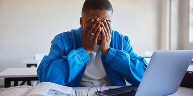 Student stressed with laptop and books.