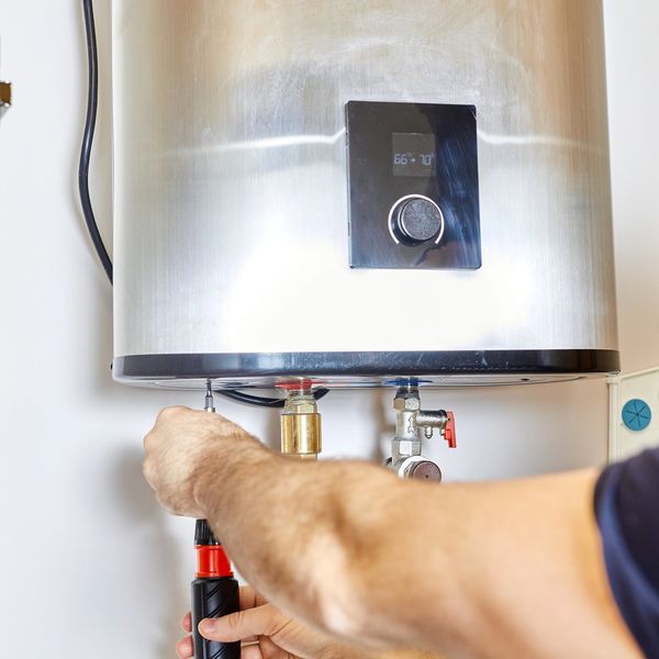 Person repairing or adjusting a modern water heater with a screwdriver.