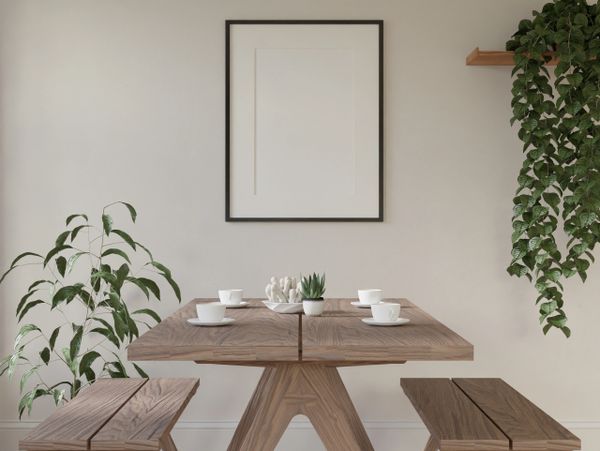 Minimalist dining area with wooden table, benches, plants, and a blank picture frame.
