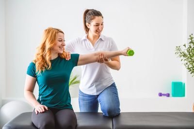 Physiotherapist teaching shoulder exercise with dumbbell.