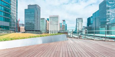 Modern cityscape with wooden deck and glass buildings under a blue sky.