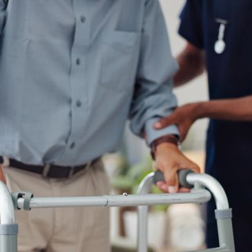 A caregiver assists an elderly man using a walker indoors.