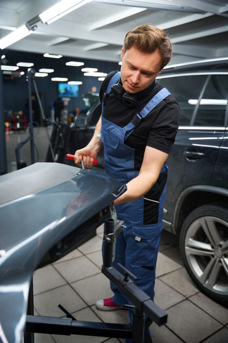 Focused collision repair technician straightening bent car fender with dent removal rod