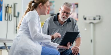 A doctor explains medical information to an elderly man using a tablet.