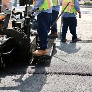Workers paving a road using heavy machinery and tools.
