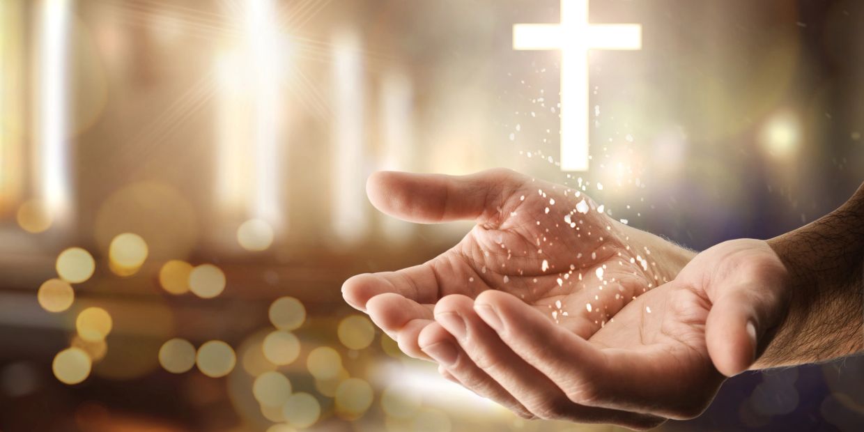 Open hands with glowing cross symbolizing faith and spirituality.