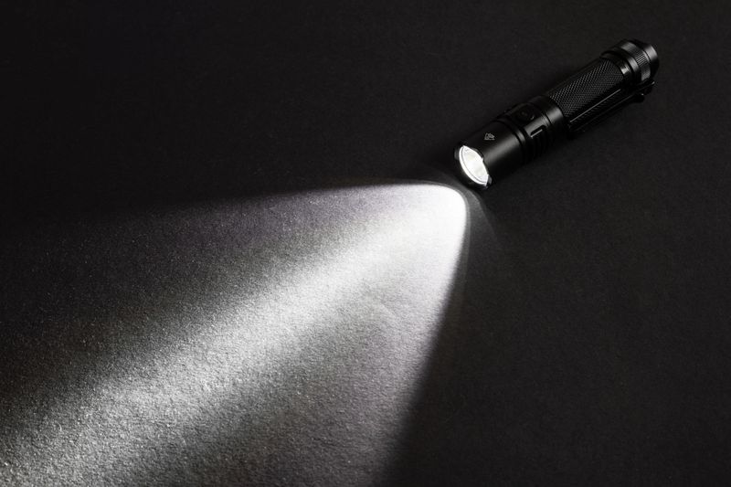 Flashlight and a beam of light in darkness. A modern led lamp with bright projection on dark wood table. Surface with copy space.