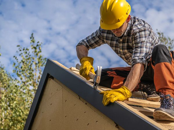 Construction worker nailing roofing materials on a sunny day.