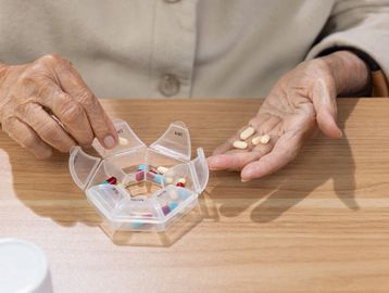 An elderly person organizing daily medications in a weekly pill organizer.