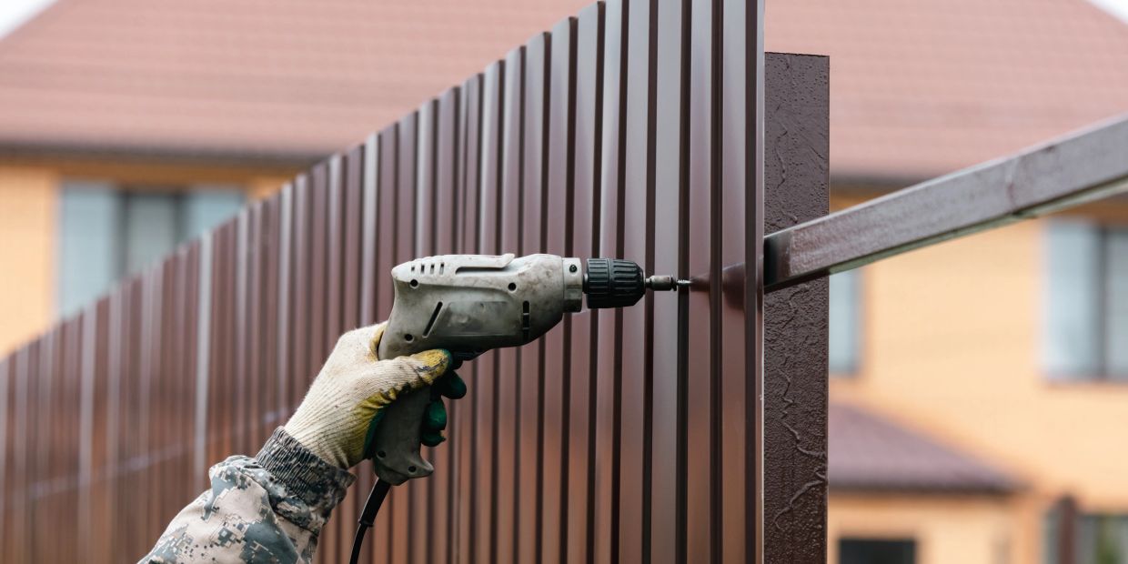 Worker drilling into metal fence panel.