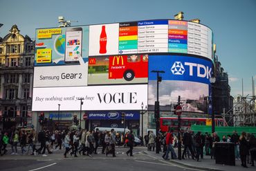 Busy urban street with large digital billboards and pedestrians crossing.